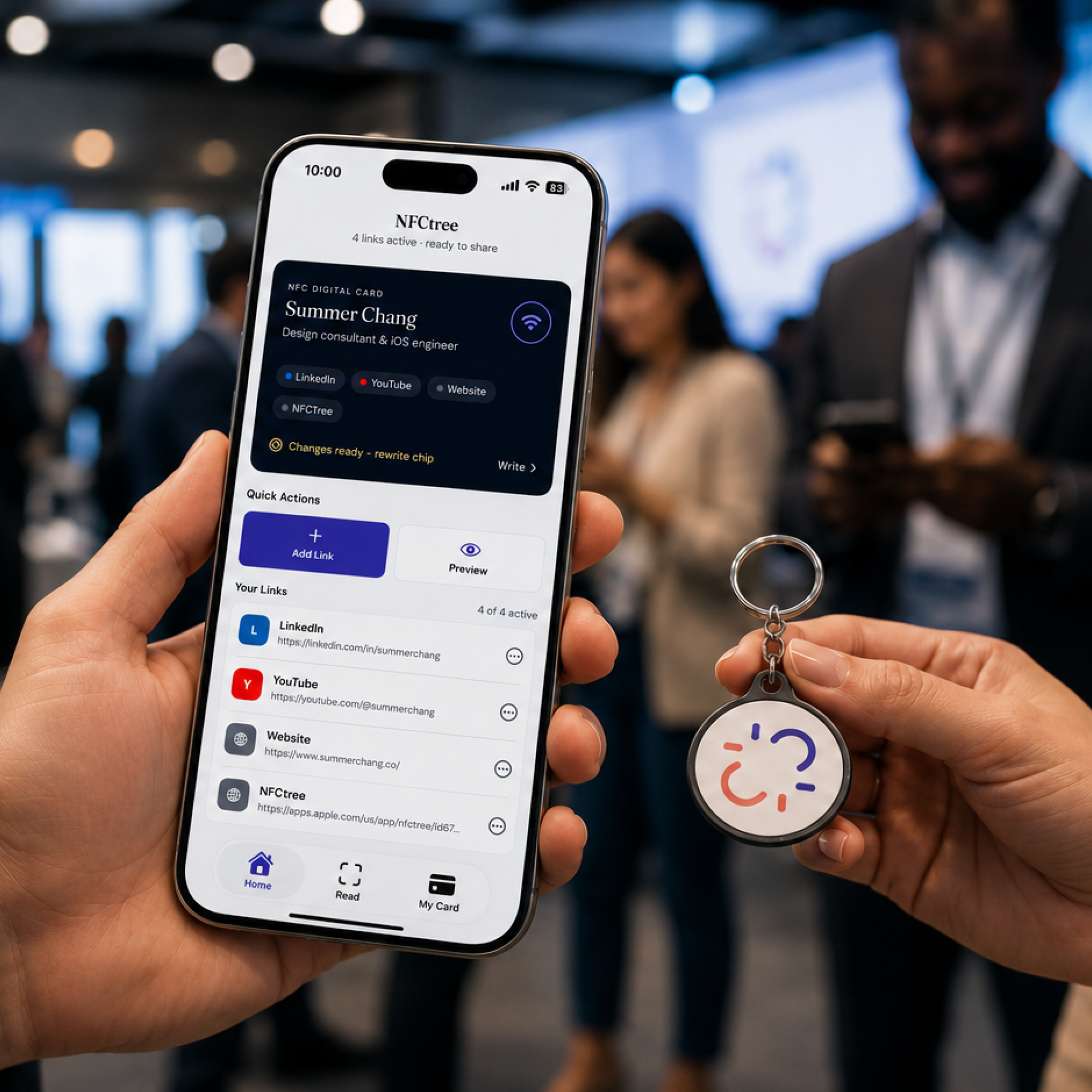 Hands holding a phone with the NFCtree app beside an NFC keychain at a networking event.